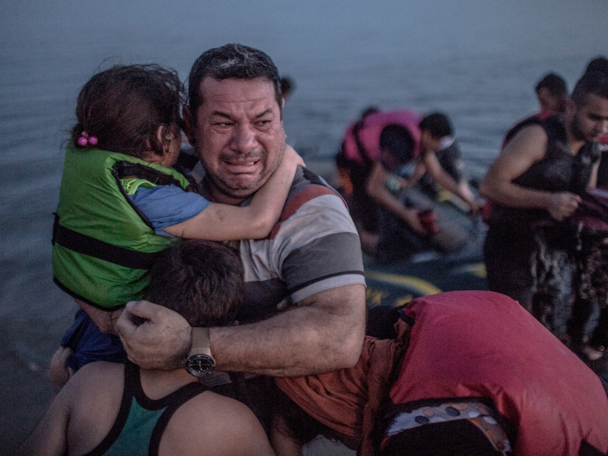 A Syrian refugee holding his son and daughter breaks out in tears of joy after arriving on the shore of the island of Kos in Greece.